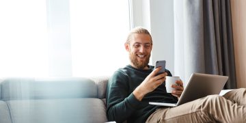 Man excitedly looking at phone and laptop